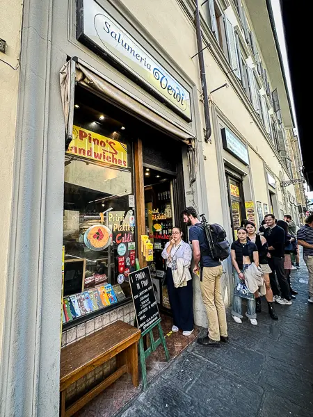 The entrance to Pino's Sandwiches, also known as Salumeria Verdi, with patrons queued outside, signaling its popularity as a go-to destination for authentic and delectable Italian sandwiches in Florence.