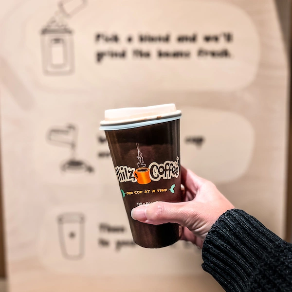 A hand holding a Philz Coffee cup with the logo, against a background featuring instructions for customizing your coffee blend.