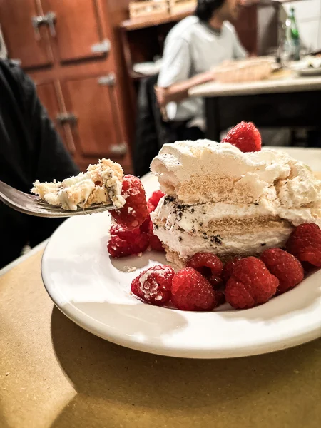 A plate of raspberry meringue cake from Trattoria Sostanza in Florence, Italy, with layers of fluffy meringue and cream, encircled by fresh raspberries.