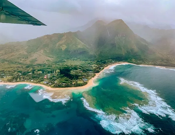 Aerial view of Kauai’s coastline with turquoise waters, sandy beaches, lush greenery, and misty mountains captured during a plane tour