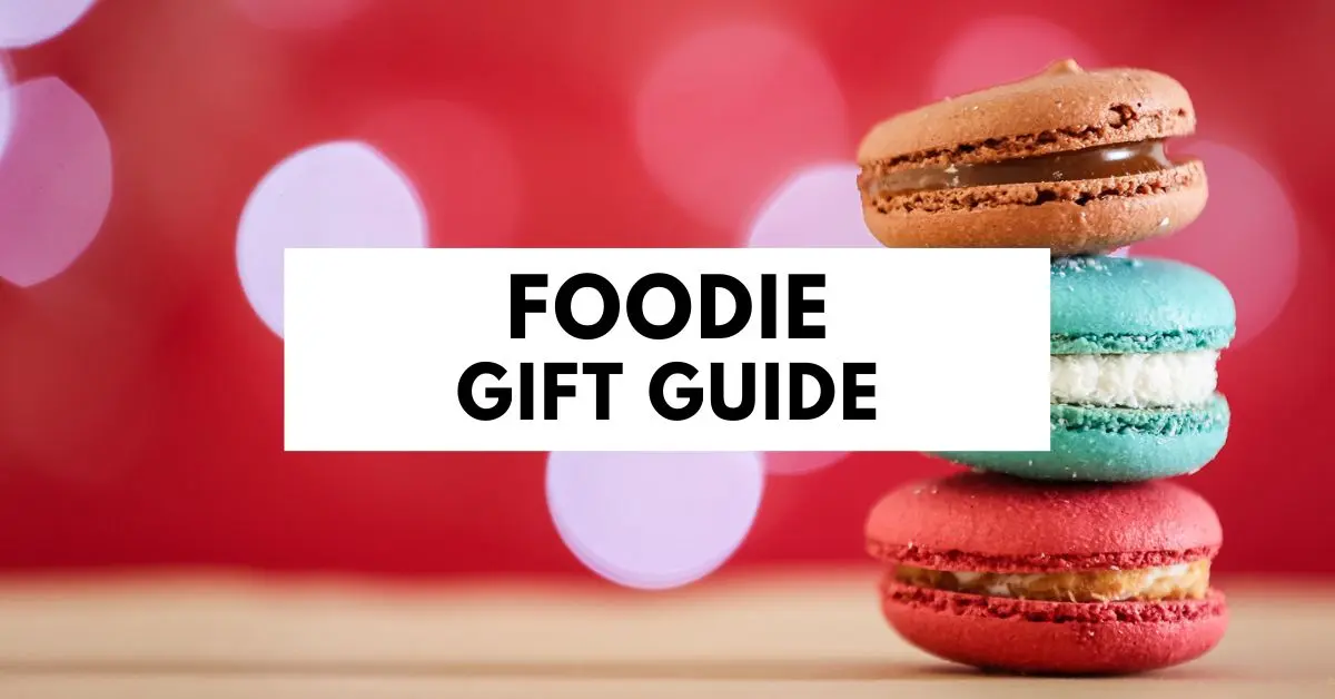 blog featured image with title foodie gift guide on image of three colorful macacons sitting atop of each other against a red background with lights