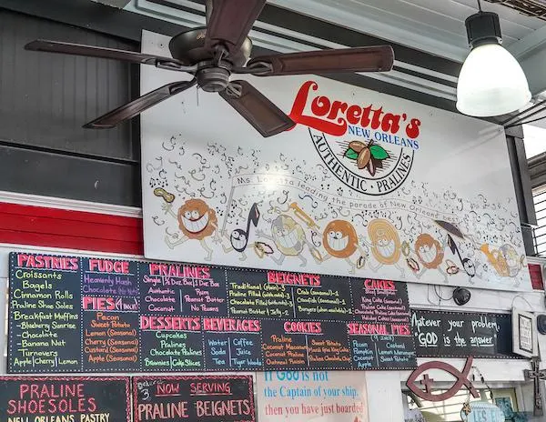 The interior of Loretta's stand at the french market featuring a colorful menu board with various offerings like pastries and pralines,.