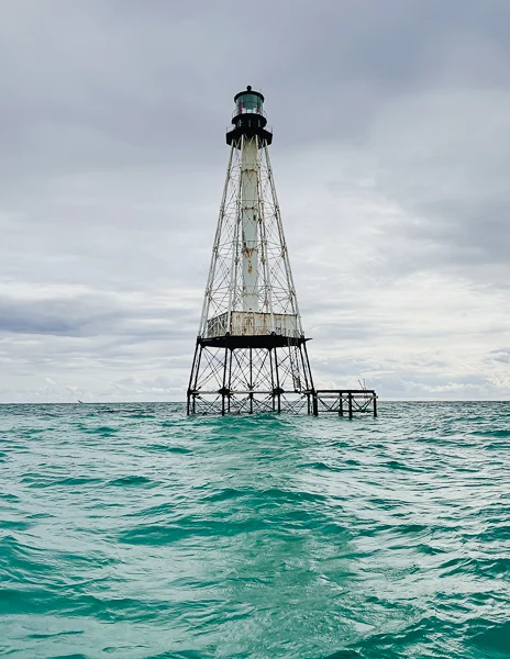 Alligator Reef Lighthouse standing tall in the turquoise waters of the Florida Keys, surrounded by cloudy skies and gentle waves.