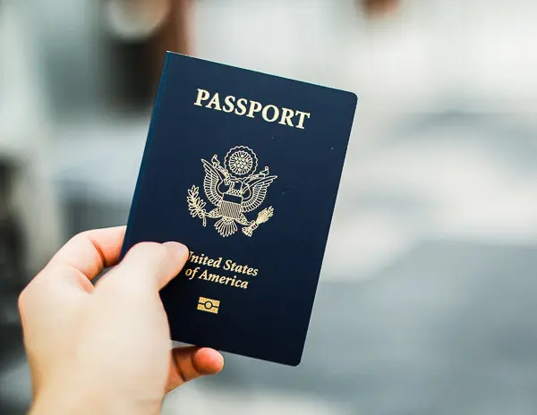 Hand holding a United States passport, one of the most important travel essentials to pack in your personal item bag.
