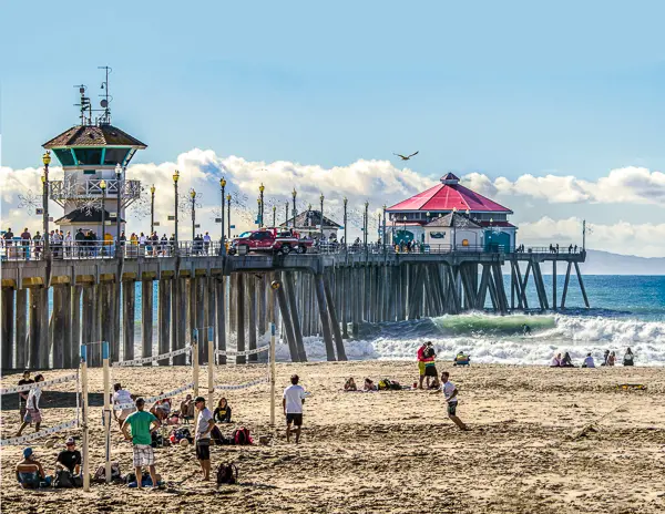 huntington beach pier in the backroud of people frolicking on the beach