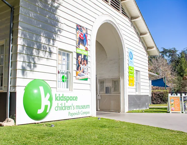 Exterior view of Kidspace Children's Museum in Pasadena, showcasing the entrance with bright signage and lush greenery around the building.