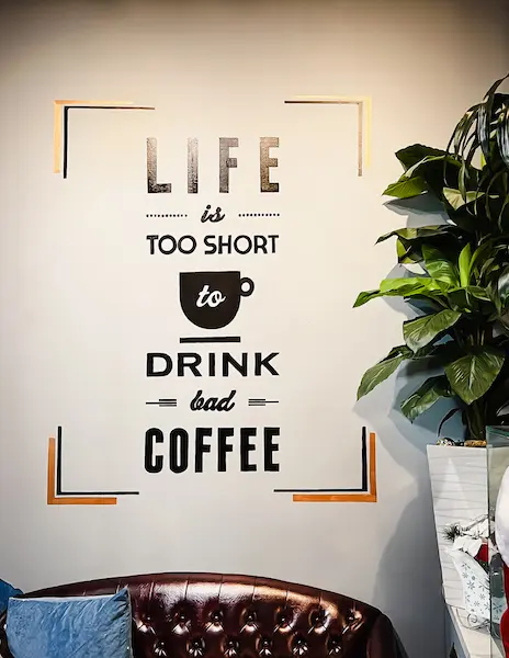 A stylish wall art sign at Republik Coffee Lounge in Pasadena that reads, 'Life is too short to drink bad coffee,' next to a lush green plant and cozy seating.