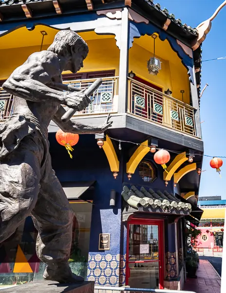 Statue of Bruce Lee in front of a colorful building decorated with red lanterns in Chinatown Los Angeles.