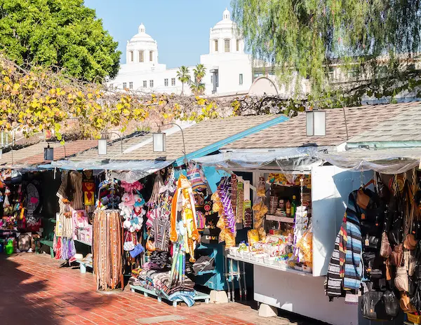 Vibrant outdoor market stalls on Olvera Street in Downtown LA, filled with Mexican souvenirs, clothing, and decor under a sunny sky.