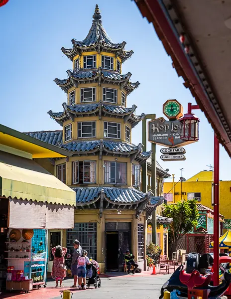View of the iconic pagoda-style Hop Louie building in Chinatown Los Angeles, with people walking nearby and vibrant storefronts around.