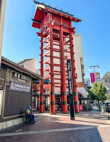 Iconic red tower at the entrance of Japanese Village Plaza in Little Tokyo, Downtown Los Angeles, with surrounding shops and signs visible.