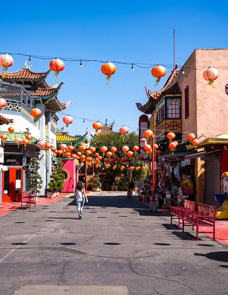 A person walks down a lantern-lined street in Chinatown Los Angeles, surrounded by colorful buildings and hanging red lanterns.