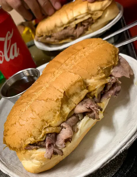 French dip sandwich at Philippe’s in Downtown LA, served on a white plate with a side of au jus and a can of Coca-Cola in the background.