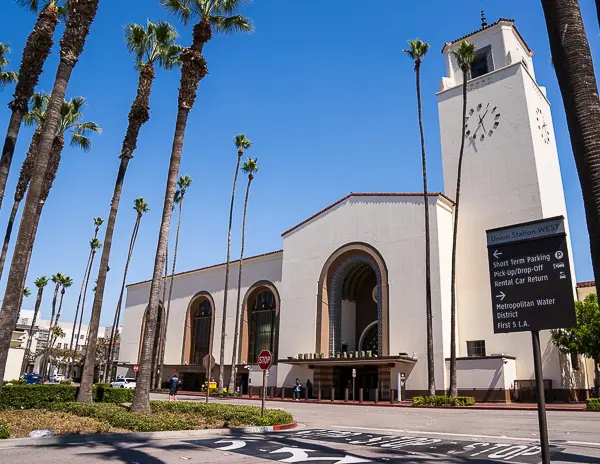 Front view of Union Station in Downtown LA, with its iconic tower, arched entrance, and palm trees lining the street.