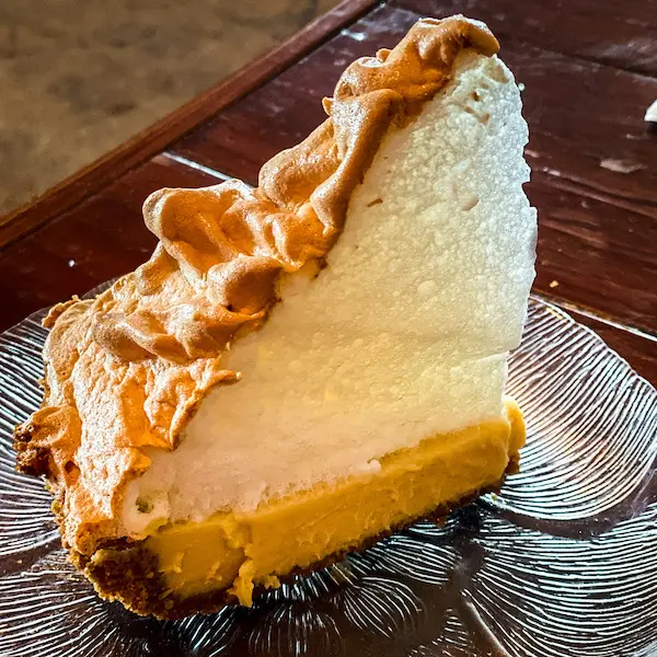 A slice of key lime pie from Blue Heaven topped with a high peak of toasted meringue, served on a patterned glass plate.