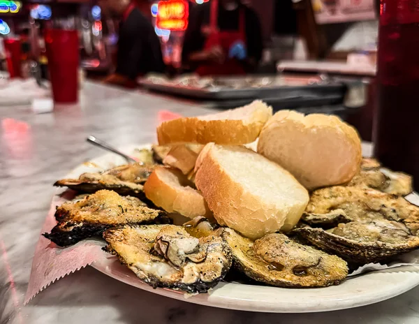 Plate of charbroiled oysters served with slices of French bread on a marble counter at Acme Oyster House in New Orleans.