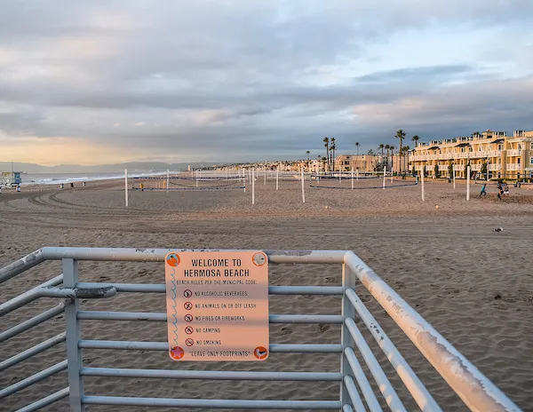 hermosa beach at sunrise, volleyball nets up in the sand and a welcome to hermosa beach sign on the railing