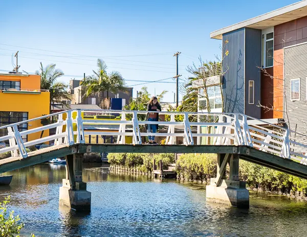 Kathy standing on a quaint wooden bridge over the serene waters of the Venice Canals in Los Angeles.