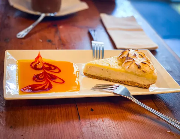 A slice of vegan key lime pie with toasted meringue topping from The Cafe in Key West, served on a white plate alongside a decorative caramel-raspberry drizzle.