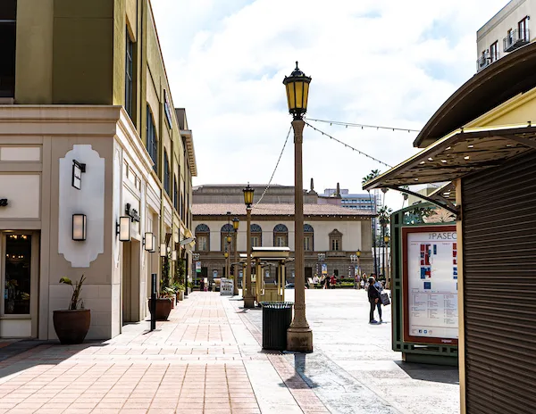 Street view of The Paseo shopping area in Pasadena, featuring colorful street lamps and a clear view of the architecture, with people walking and a directory sign visible in the distance.