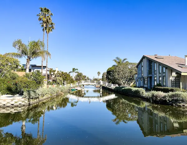 white bridge over canal, palm tree and a house in the corner