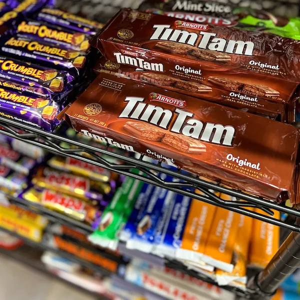 Tim Tam biscuits and other international candy brands displayed on metal shelves inside the store.