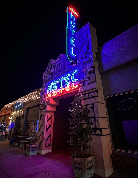 Nighttime view of the Aztec Hotel in Monrovia with its bold neon sign glowing in blue and red, highlighting the building’s Mayan-inspired architecture.