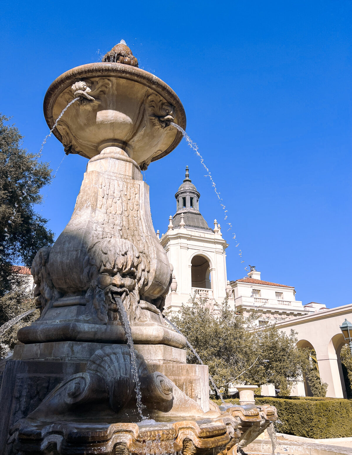 A close-up of the ornate fountain in front of Pasadena City Hall, with water flowing and the beautiful building visible in the background.