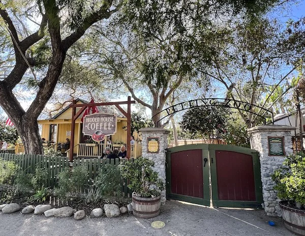 outside of hidden coffee house, big tree shading a yellow house and patio with a gate that says petting zoo