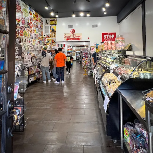 Interior view of Sweet Ethans candy shop with colorful displays, candy counters, and customers browsing.