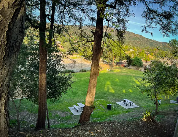 View of Kiwanis Park in Monrovia with picnic tables, open grassy space, and mountain views framed by tall trees.
