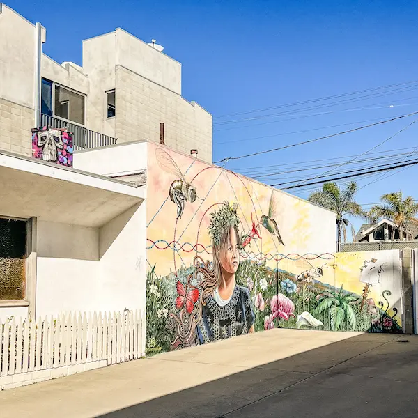 Large mural of a young girl surrounded by flowers, butterflies, and hummingbirds on the side of a building in Venice Beach.