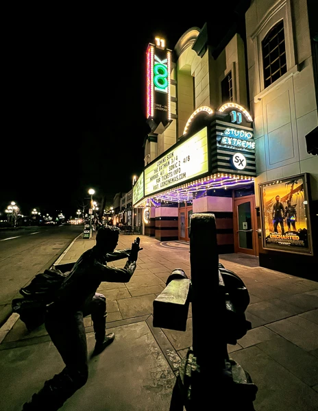 statue of director and film camera next to old school movie theater