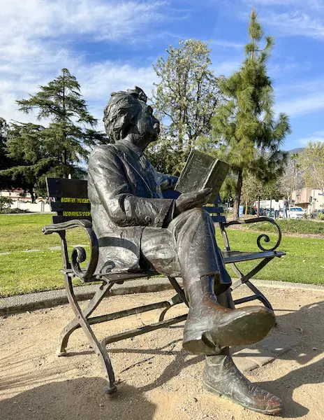 Bronze statue of Mark Twain sitting on a bench reading a book at Library Park in Monrovia.