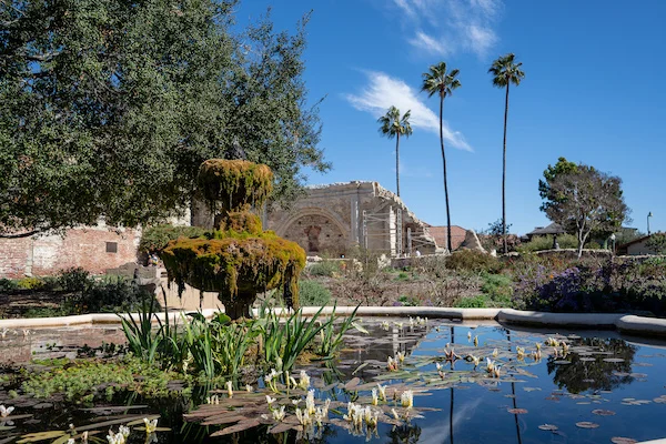 fountain with flowers, palm trees and ruins in the background