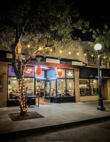 Exterior of Monrovia Ramen at night with glowing red lanterns, string lights, and sidewalk seating.