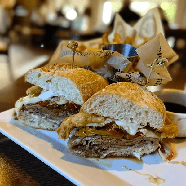 A hearty Parisian Prime sandwich filled with sliced beef, onions, peppers, and horseradish aioli, served with fries and au jus at Trevor on the Tracks.