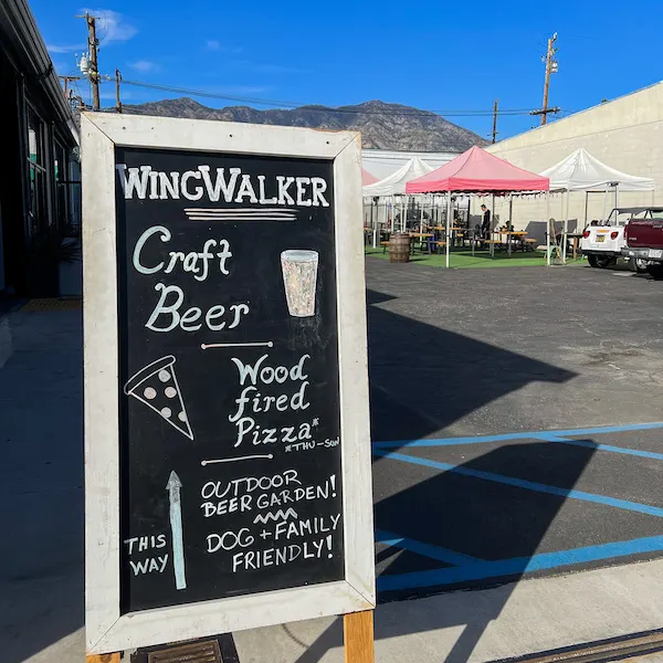 Chalkboard sign outside Wingwalker Brewery advertising craft beer, wood-fired pizza, and their outdoor beer garden.