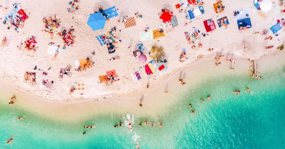 featured image without text | beach trip packing list | aerial view of a beach with many beachgoers relaxing and swimming for the day