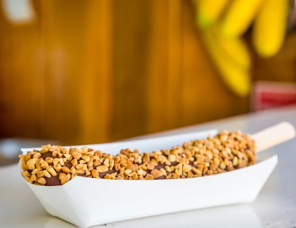 Chocolate covered frozen banana covered in peanuts