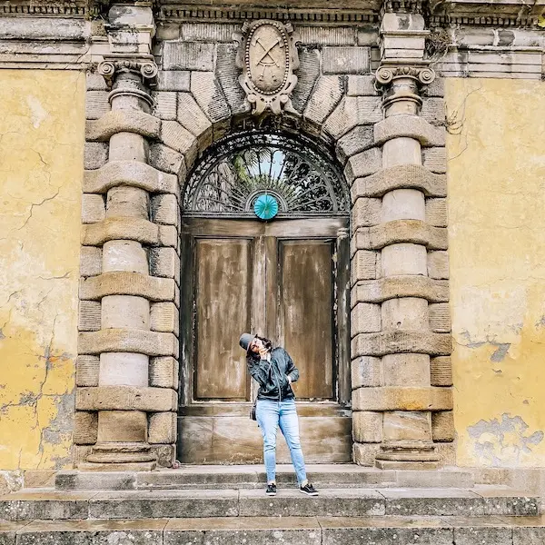 woman standing in front of old wooden door and archway made of stones with a yellow facade