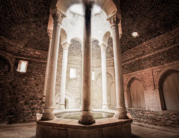 Historic Arab Baths in Girona, Spain, featuring Romanesque-style stone columns and a central skylight illuminating the space.