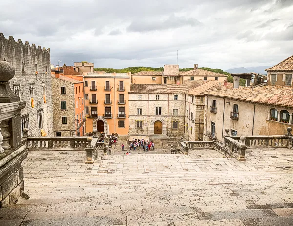 A scenic view from the top of Girona Cathedral's steps, overlooking a historic square with colorful buildings and a group of tourists gathered below.