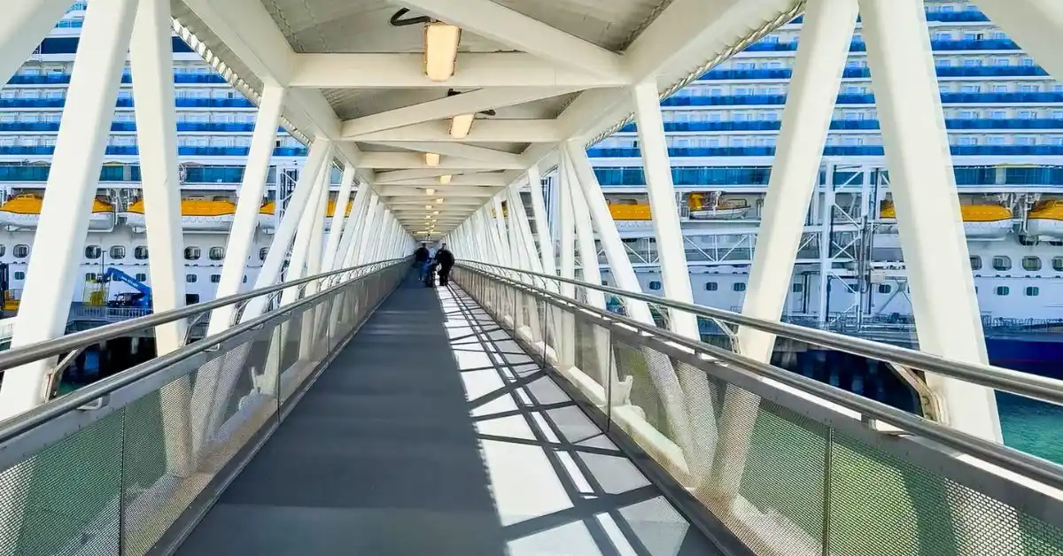 featured image: Passengers walking down a covered gangway toward a cruise ship on embarkation day, a fitting image for cruise embarkation day tips.