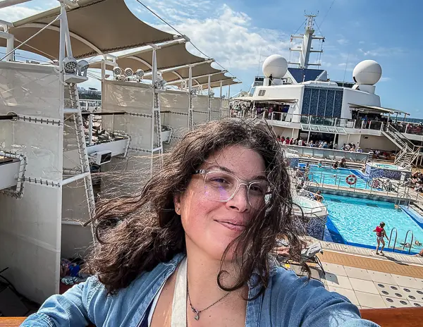 Cruise passenger (kathy) taking a selfie on the pool deck during embarkation day, enjoying the sunshine and relaxed atmosphere before sail away.