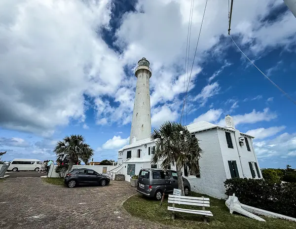 Gibb’s Hill Lighthouse in Bermuda with the white lighthouse tower, surrounding buildings, and cloudy blue sky.