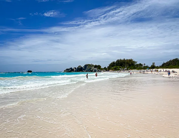 Horseshoe Bay Beach in Bermuda with pink sand, turquoise water, waves, and beachgoers along the shore.