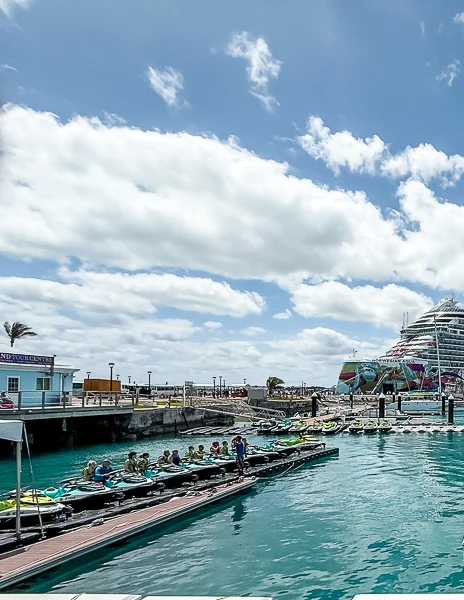 Jet ski tour group leaving Royal Naval Dockyard in Bermuda with turquoise water and a cruise ship in the background.