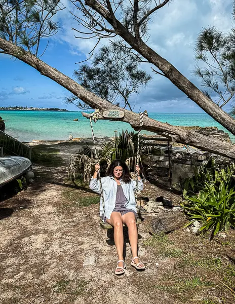 Woman (Kathy) sitting on a swing at Glass Beach in Bermuda with turquoise water and shoreline in the background.