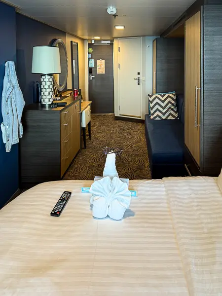 Quantum of the Seas cruise cabin with bed, seating area, storage, and towel animal